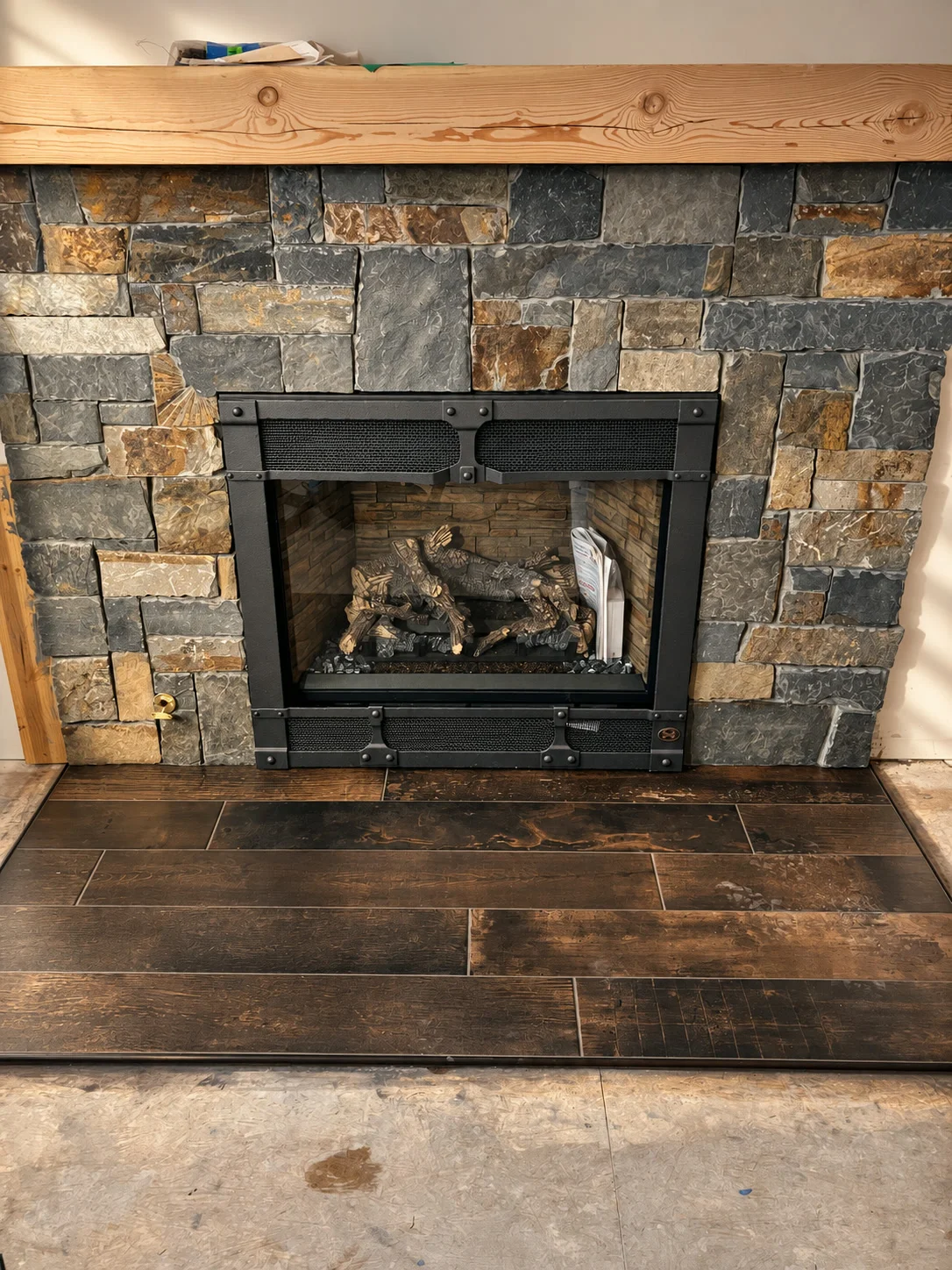 Rustic natural stone fireplace with reclaimed timber mantle and tile hearth