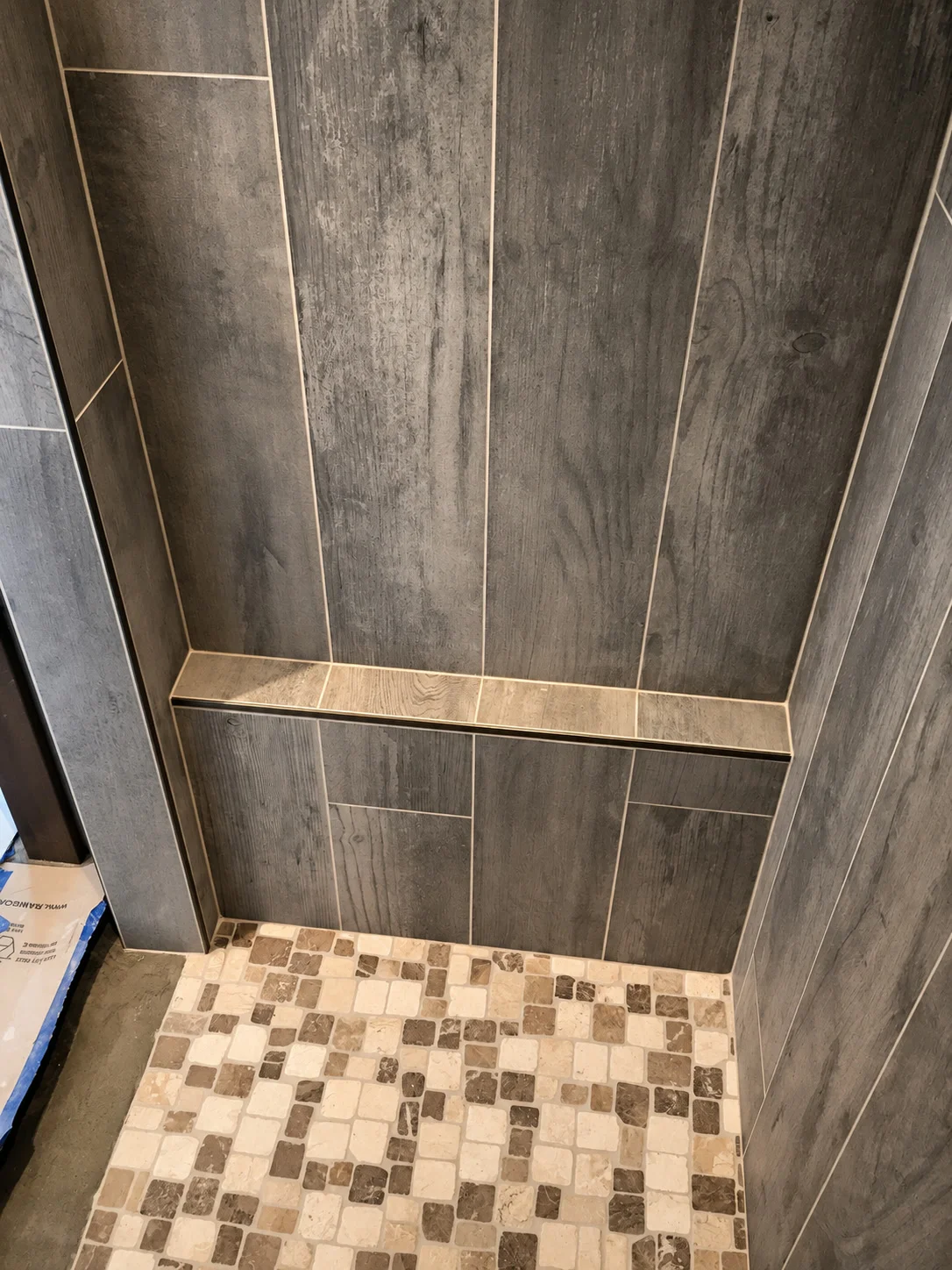 Walk-in shower with vertical wood-tone tile, floating bench, and pebble floor