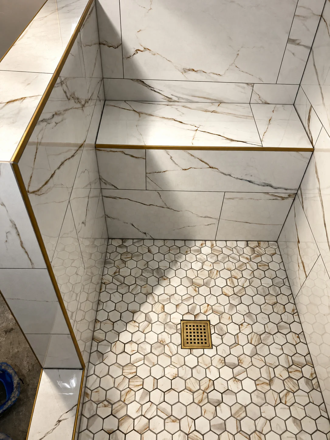 Calacatta marble tile shower with brass trim, floating bench, and hex floor